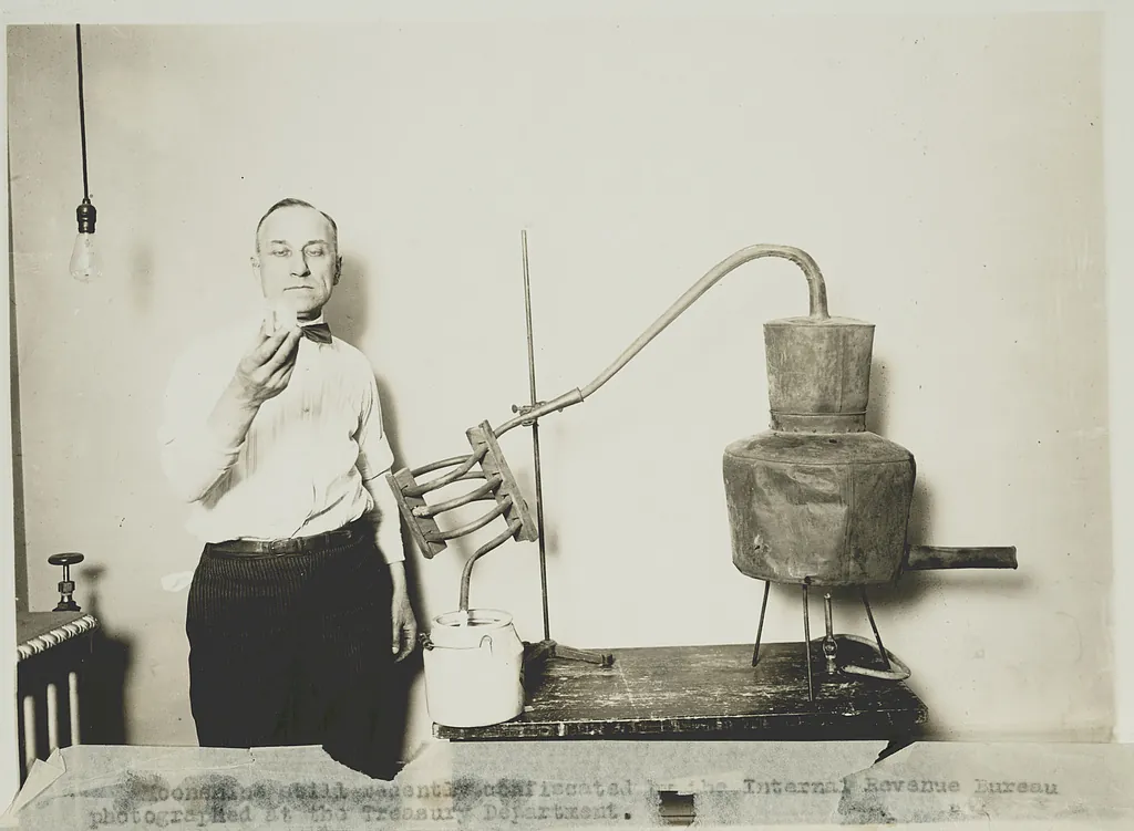 A man holds up a cup beside a confiscated copper moonshine still